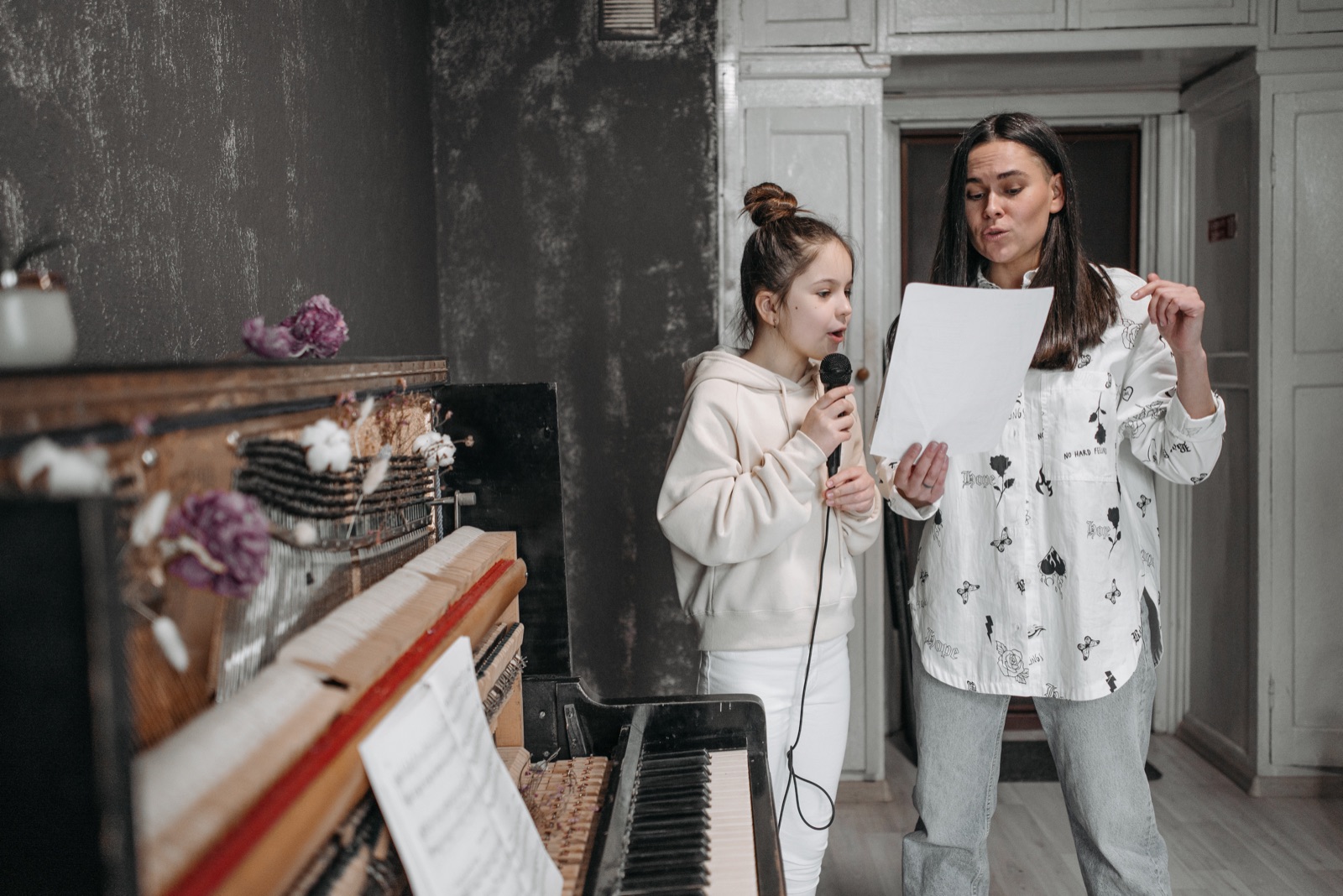 A young singer practising a song with a teacher beside a piano
